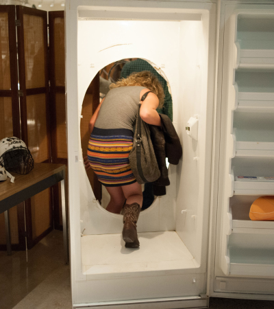 person walking through a hole cut in the back of an open refrigerator