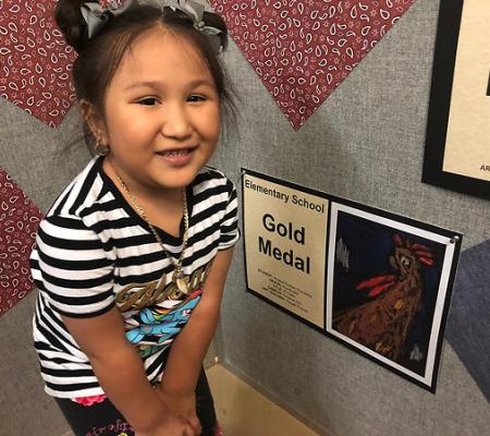 girl standing next to medal-winning artwork