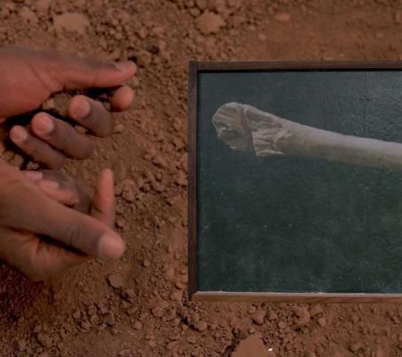 Ariel Rene Jackson and Michael J Love participate in SXSW arts program with their performance The Future is a Constant Wake depicted in this image of hands above a green chalkboard among red dirt