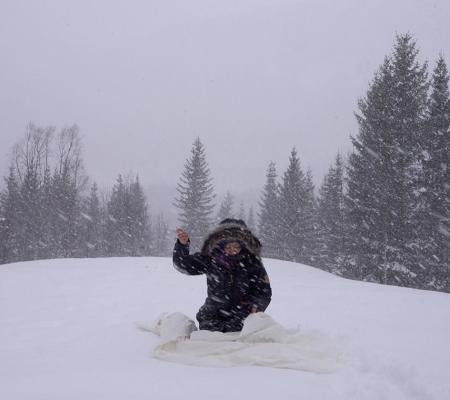 woman sitting in snow in front of trees sewing