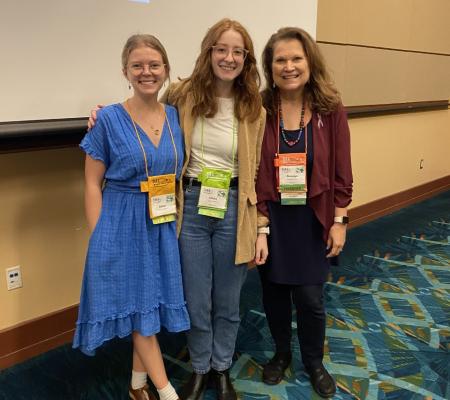 three women standing in front of their presentation at a conference