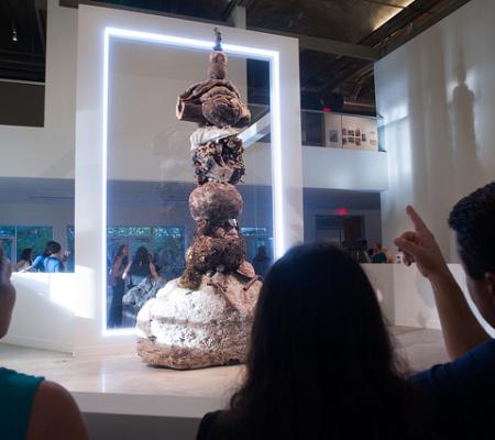students in the foreground looking at stacked burl installation in background