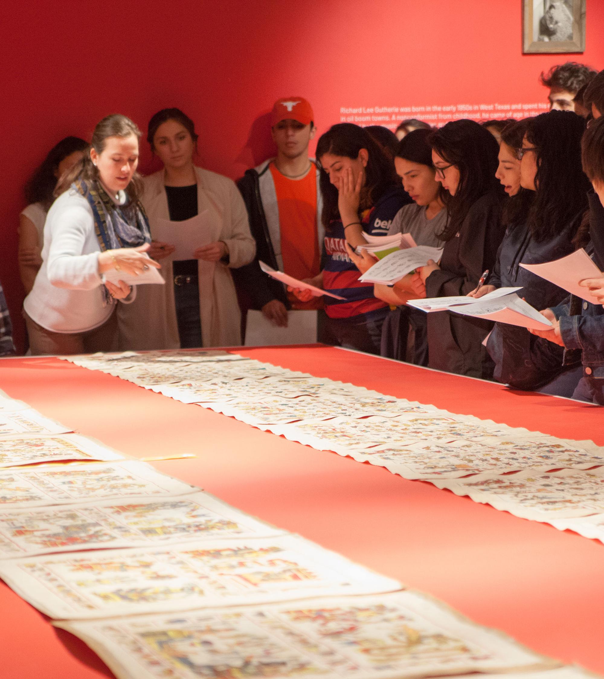 people standing around table looking at scrolled prints